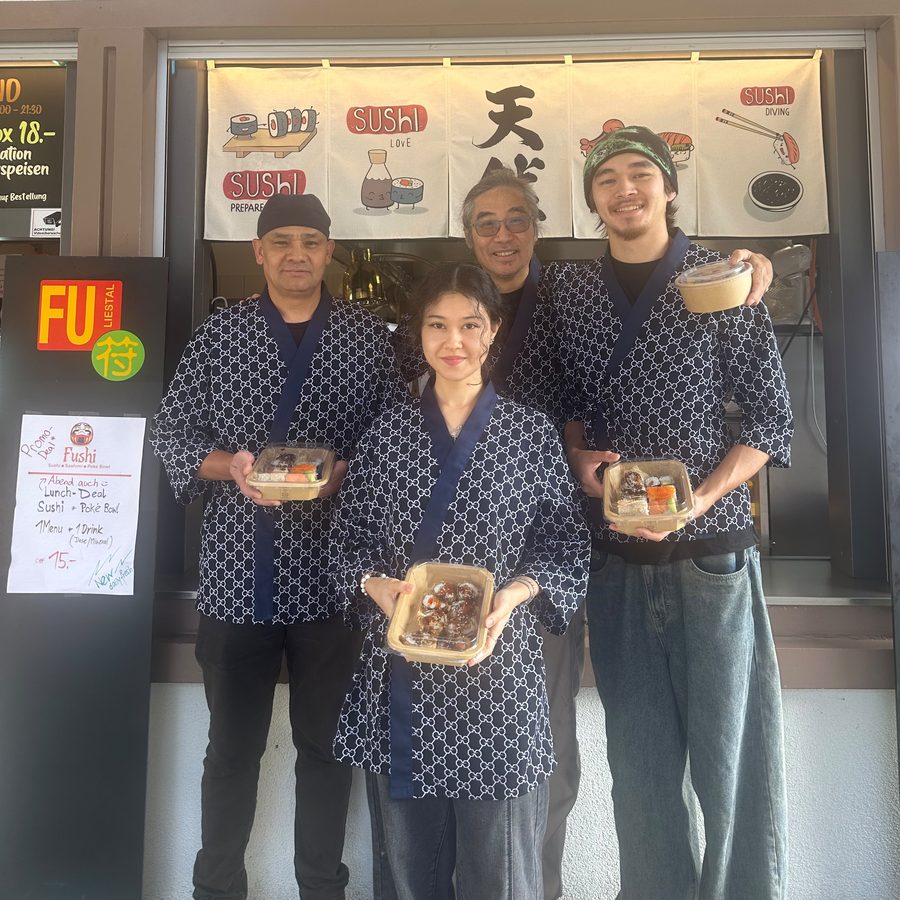 Das Fushi-Team vor dem Stand an der Poststrasse 1 in Liestal: vier Personen in dunkelblauen Jacken mit weissem Muster, in den Händen Sushi-Boxen und eine Poké Bowl